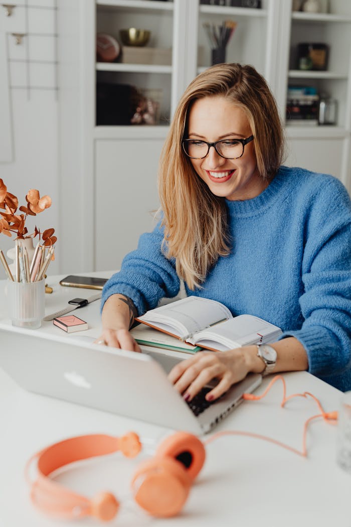 Home A cheerful woman in a blue sweater working remotely with a laptop in a cozy home setting.